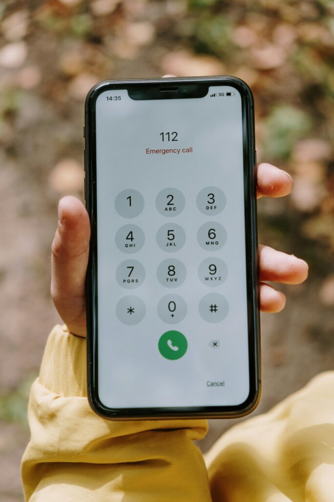 Close-up of a hand holding a smartphone displaying emergency call screen outdoors.